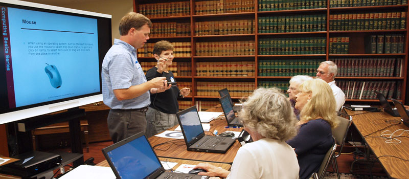 Library technology trainers demonstrate the use of a mouse in a computer class